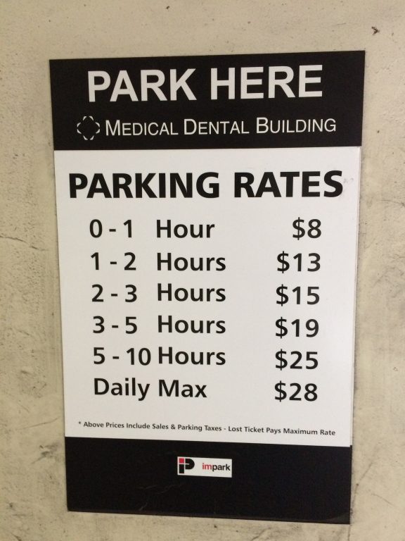 A sign at the Medical Dental Building lists parking rates: 0-1 hour $8, 1-2 hours $13, 2-3 hours $15, 3-5 hours $19, 5-10 hours $25, daily max $28. Taxes included; lost ticket pays max rate.